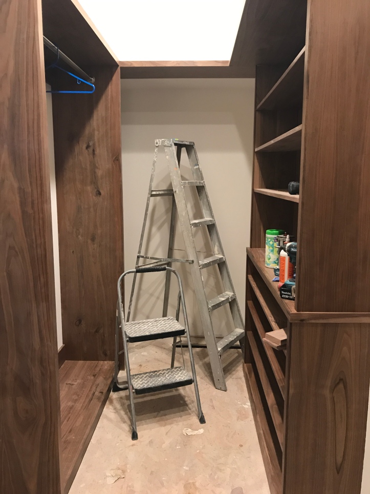 Walnut closet built in shelves in a room with unfinished floors and two ladders.