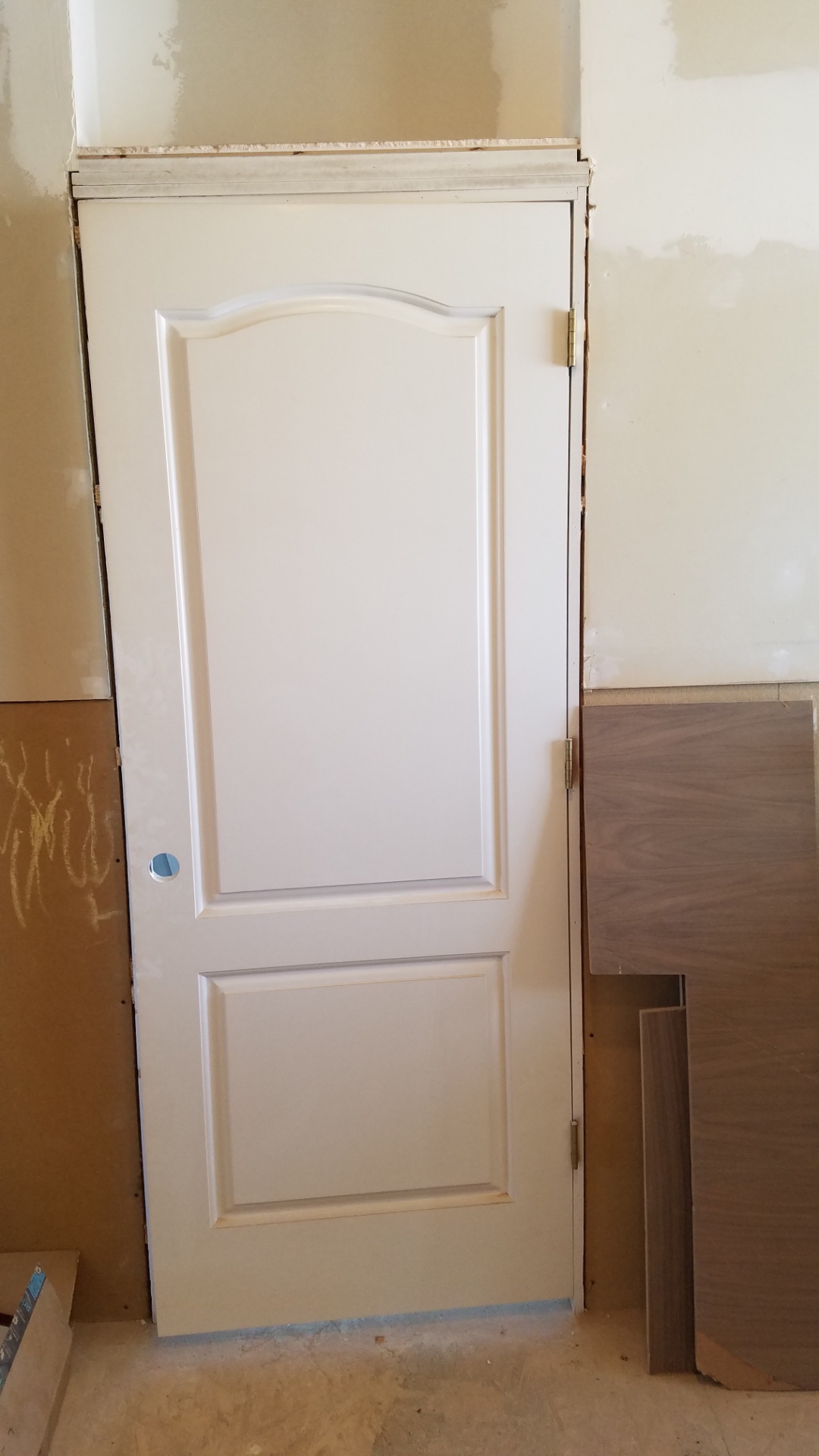 A white solid wood door with a fresh coat of paint hung in a door frame in an unfinished room with sound board on the walls