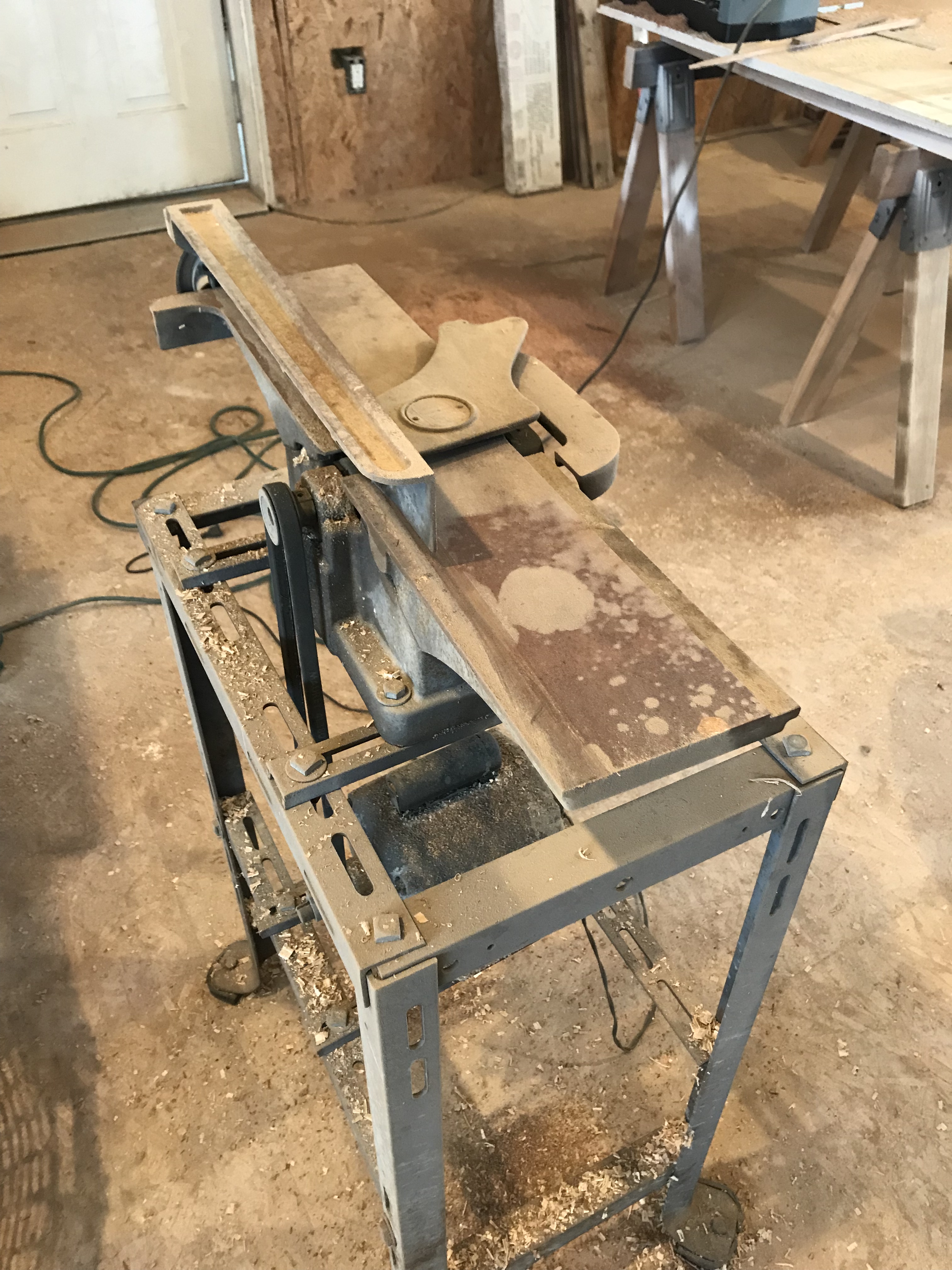 Old jointer used in woodworking sitting in a work shop with saw dust and wood chips dusted on it