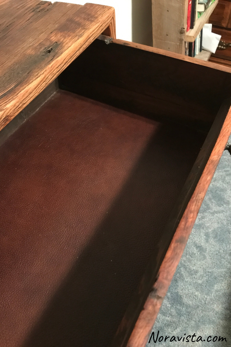 The top drawer of a cabinet pulled out to reveal brown leather lining on the bottom of the drawer