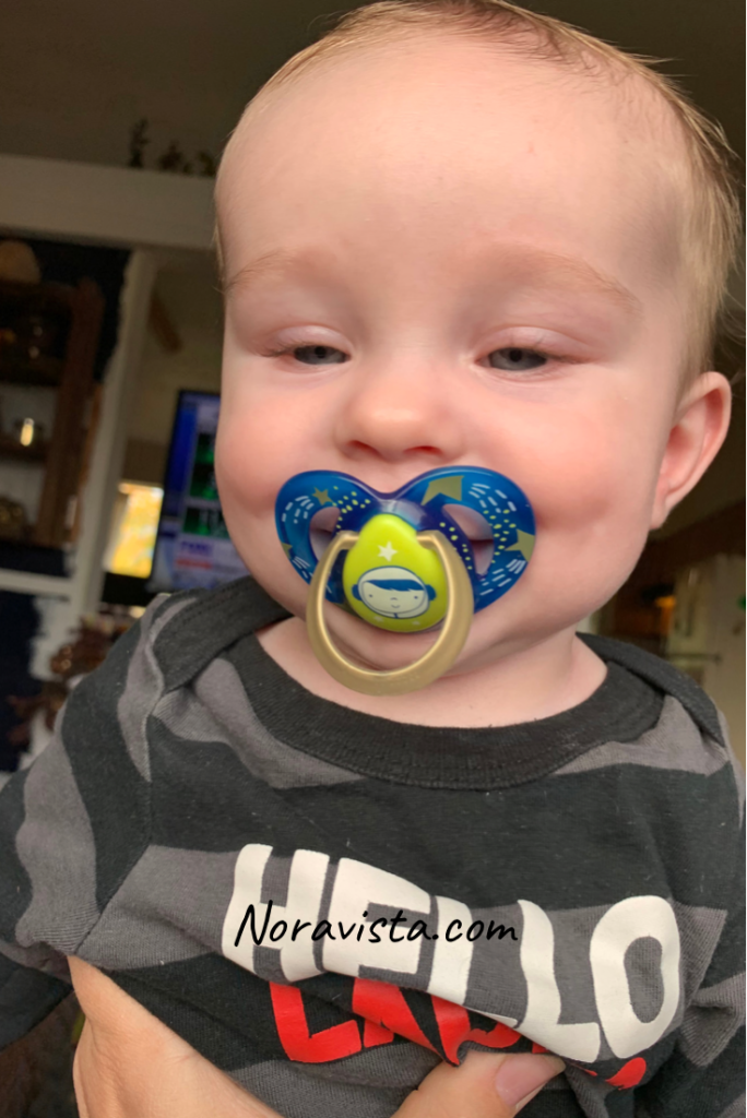 Blonde baby boy with a blue binkie in his mouth and smiling